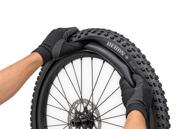 Illustrative gloved hands fitting an inner tube into a Maxxis Rekon+ tyre