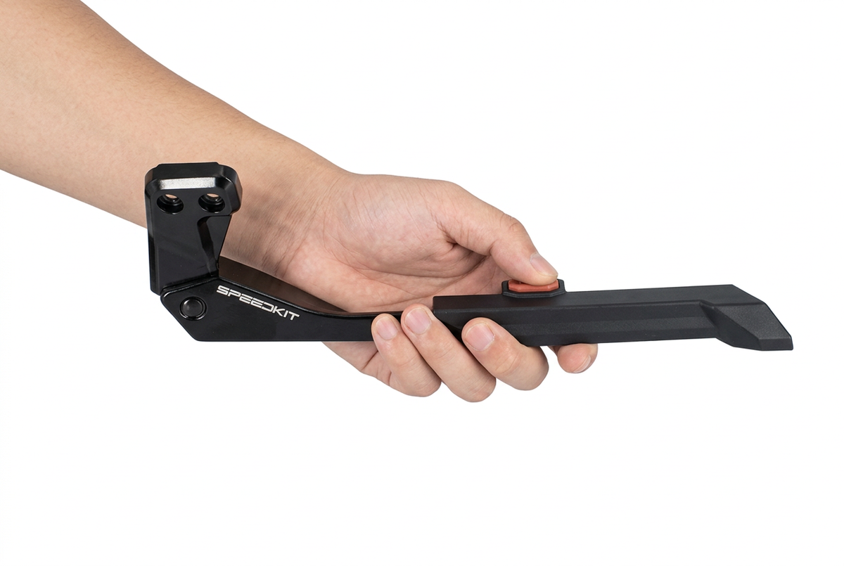 A hand holding a black Speedkit handlebar clamp and extension bar with a small orange accent button, shown against a plain white background. 2