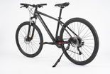 A black mountain bike with a black frame, black tires, and a black kickstand, photographed on a seamless white studio background. 4
