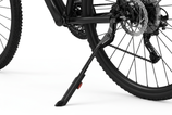 Close-up of a bicycle's rear wheel and black kickstand on a clean white background, showing the stand supporting the frame near the wheel hub.
